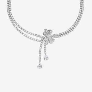 A sparkling diamond necklace with two strands converging at a floral-shaped cluster. The cluster features a bow-like design accented by two dangling pear-shaped diamonds. The background is a plain, light color.