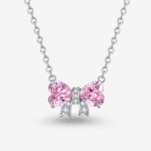 A silver necklace with a bow-shaped pendant. The bow features two pink heart-shaped gemstones as loops and small white stones lining the knot, against a plain white background.