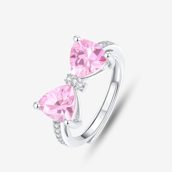 This playful design showcases a silver ring featuring two large, triangular pink gemstones set side by side like a charming bow. The band sparkles with small clear stones, enhancing its elegance against a plain white background that highlights the ring's intricate details.