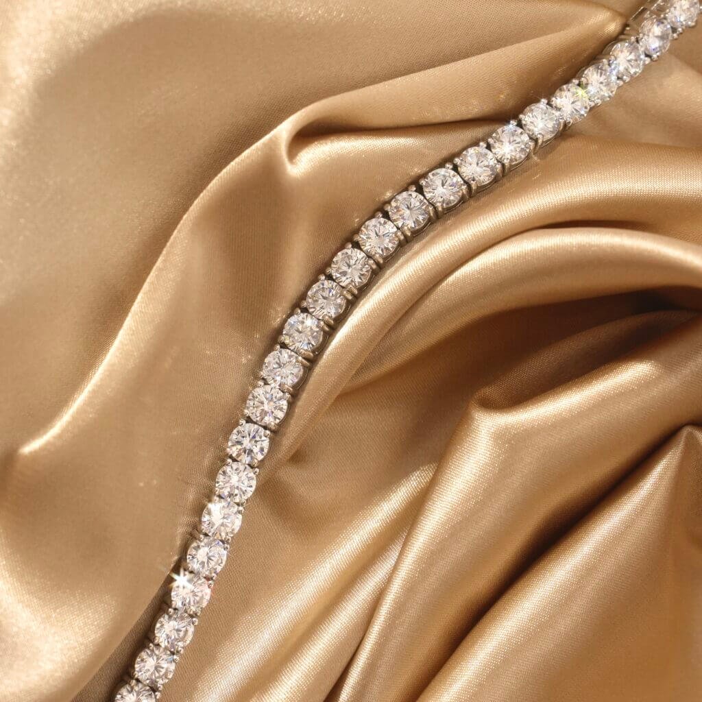 A dazzling diamond bracelet elegantly displayed on luxurious, shimmering gold satin fabric. The round diamonds are closely set, creating a stunning contrast against the rich textile.