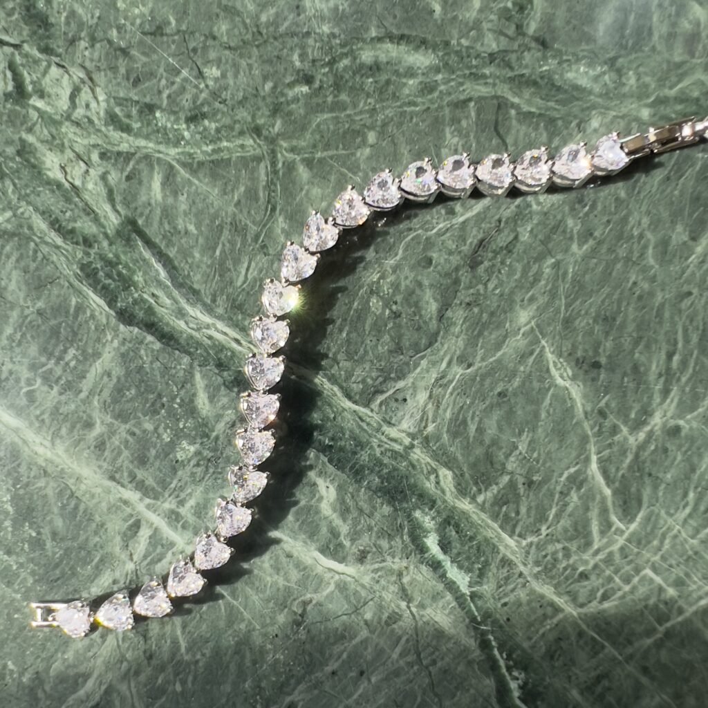 A elegant bracelet featuring teardrop-shaped diamonds is placed on a textured green marble surface. The bracelet sparkles under the light, showcasing its intricate design and shimmering stones.