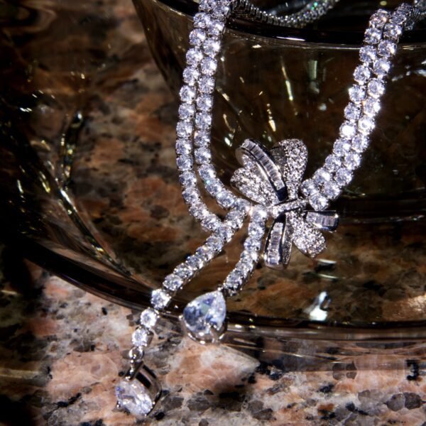 A sparkling diamond necklace with two strands and a floral design centerpiece, adorned with a teardrop-shaped pendant, rests on a textured marble surface.