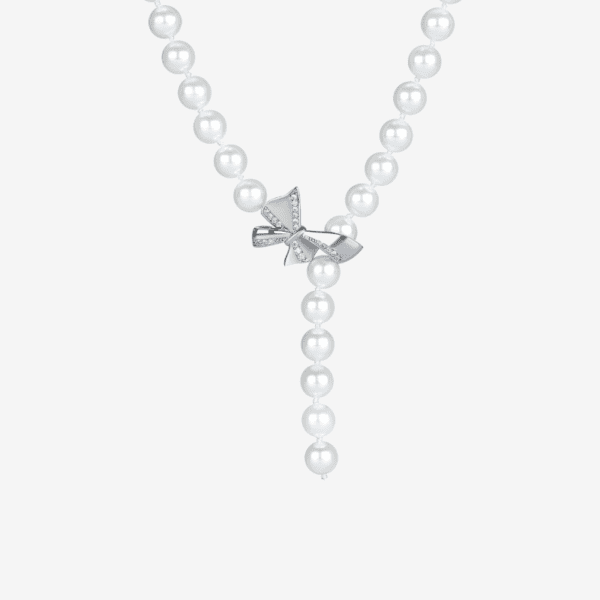 A pearl necklace with a string of round pearls forms a Y-shape, centered by a silver bow adorned with small, clear gemstones. The necklace is displayed on a plain white background.