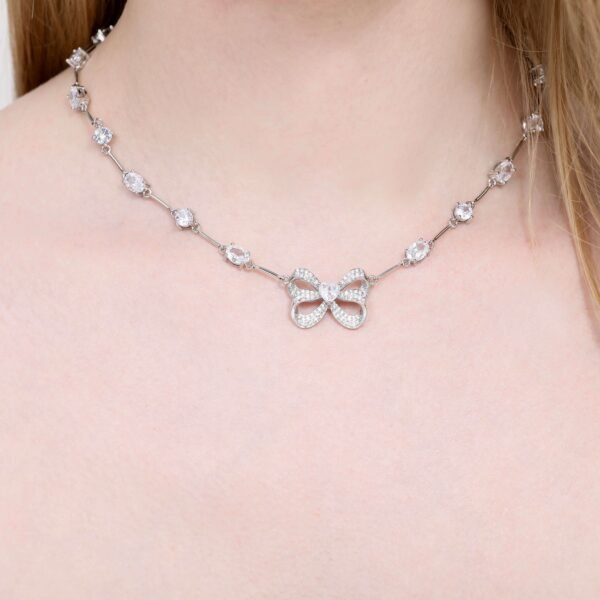 A person wearing a delicate necklace with a bow-shaped pendant. The necklace features intricate links adorned with small gemstones, complementing the elegant design.