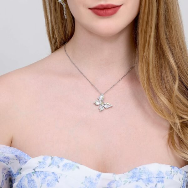 A woman with long blonde hair wearing a strapless, floral-patterned dress and a silver butterfly necklace. She is standing against a light background.