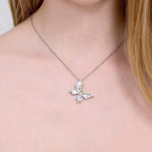 A close-up of a person wearing a silver necklace with a butterfly pendant. The pendant features white stones and is detailed with small accents. The person has long, light brown hair, and their upper chest and necklace are in focus.