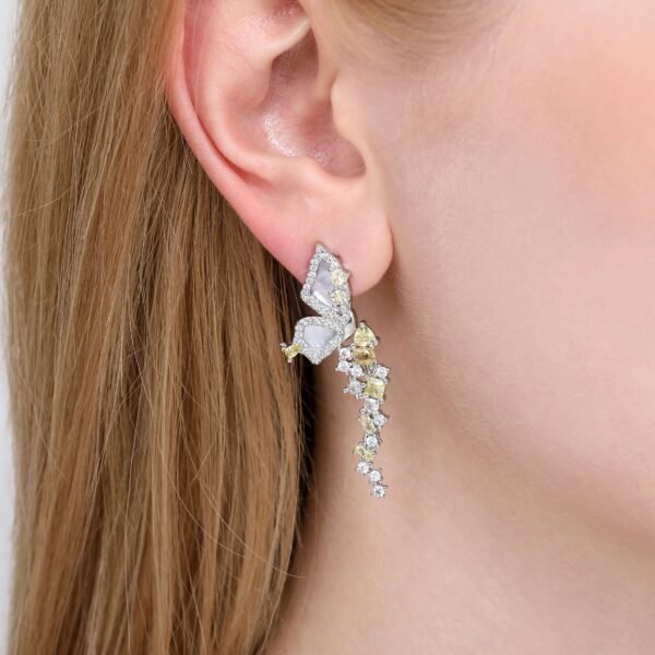 A close-up of a persons ear wearing an intricate earring featuring butterfly designs with a mix of white and yellow stones. The earring drapes elegantly down the earlobe.