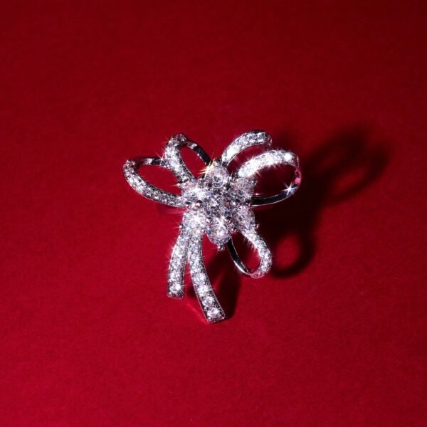 Silver diamond ring in the shape of a bow, placed on a deep red background. The ring sparkles with numerous small diamonds, adding elegance and shine.