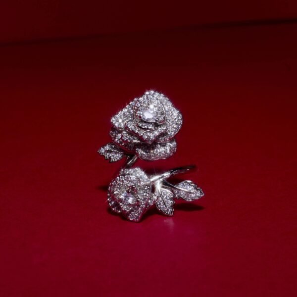 A silver ring with a floral design, featuring roses adorned with sparkling diamonds, is displayed against a deep red background.