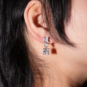 A pair of elegant silver earrings with square and round clear gemstones, featuring a swirled silver backing and a drop design against a white background.